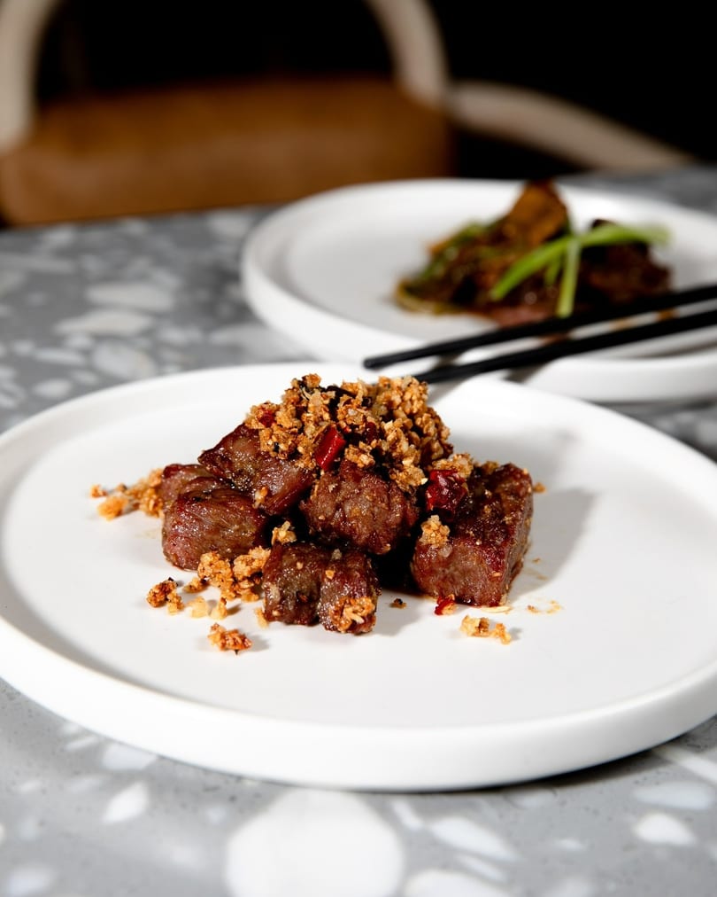 Close-up of diced beef with crispy garlic and chili flakes on a white plate.